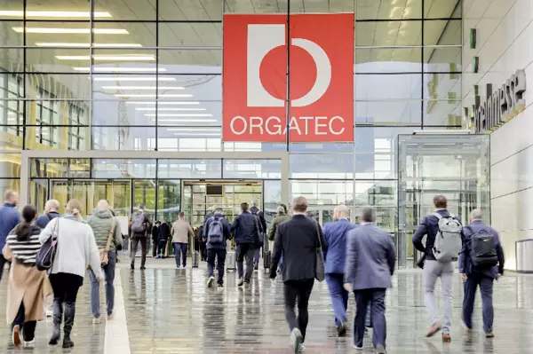 People walk to the entrance of a spacious building with a red sign saying "Orgatec"